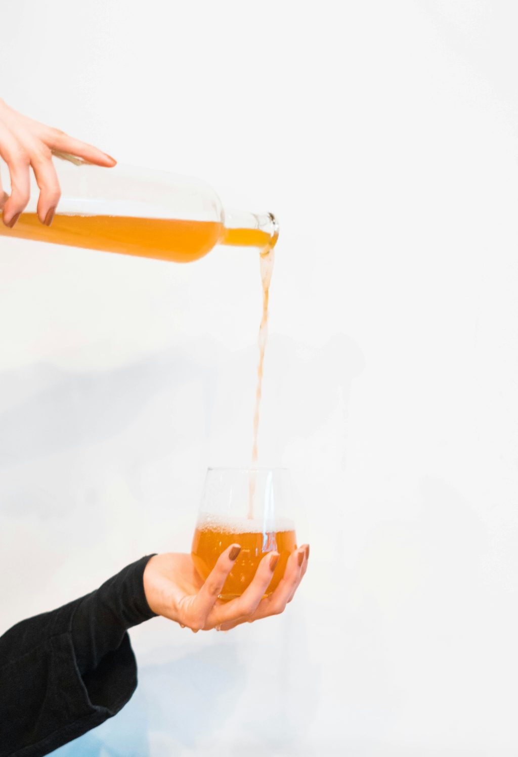 Pouring home made cider into a wine glass against a white background